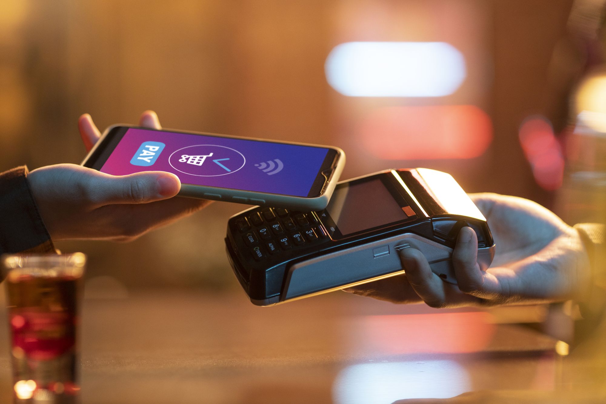 Person tapping a stablecoin credit card at a point-of-sale terminal while holding a smartphone showing a USDC wallet balance, illustrating seamless crypto payments